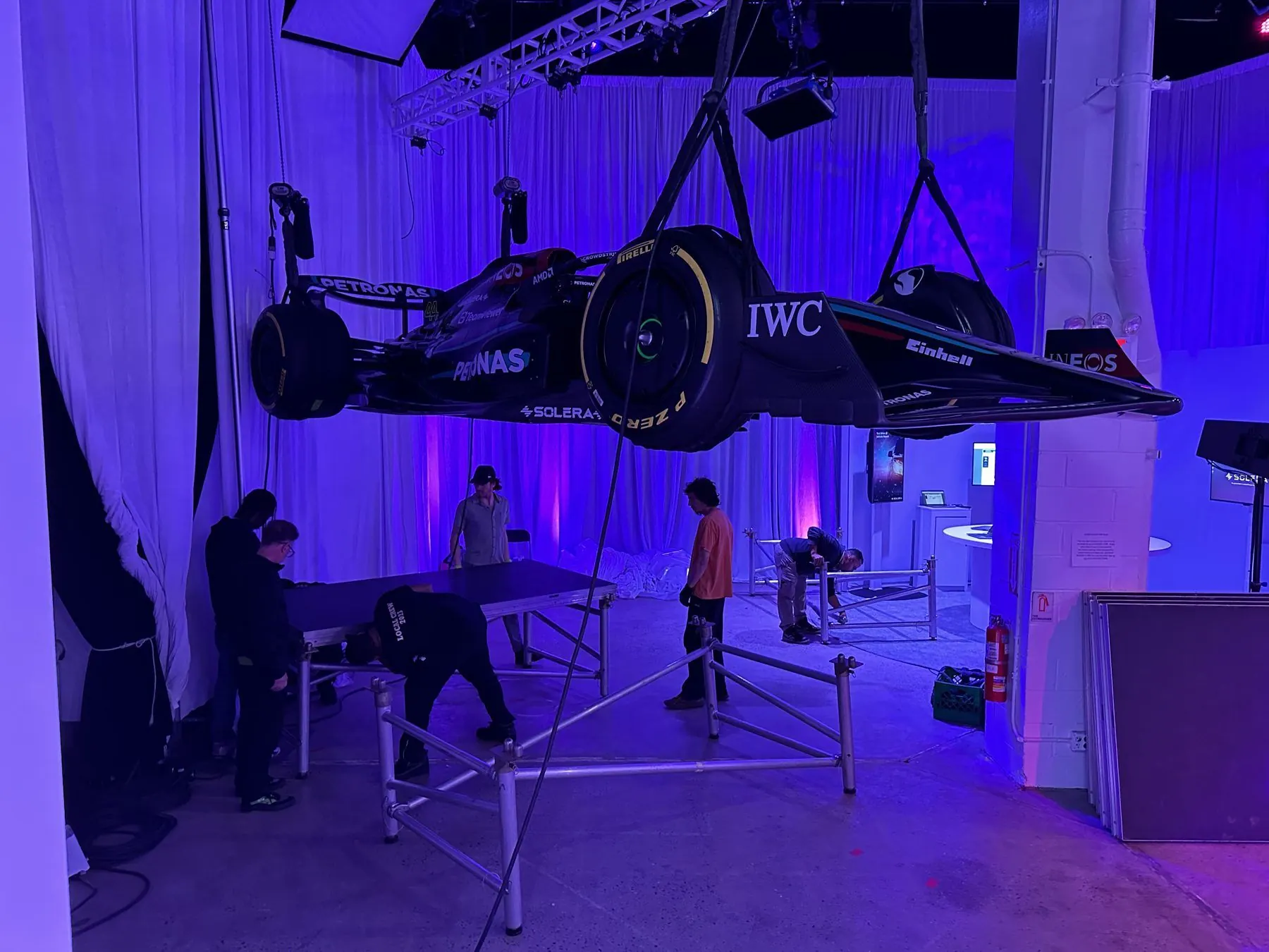 Crew building staging under a race car flown from the truss