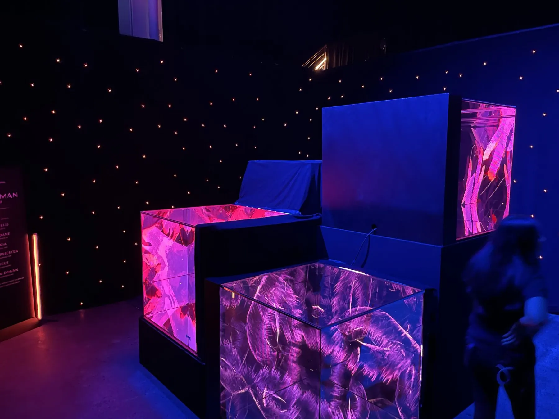 Immersive LED cube installation glowing magenta and violet against a starfield drape