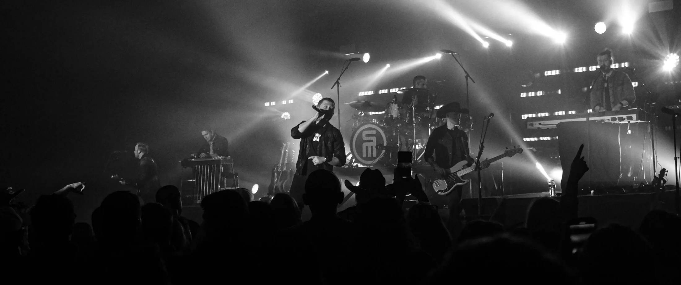 Scotty McCreery on stage under white beams, seen over the crowd in black and white