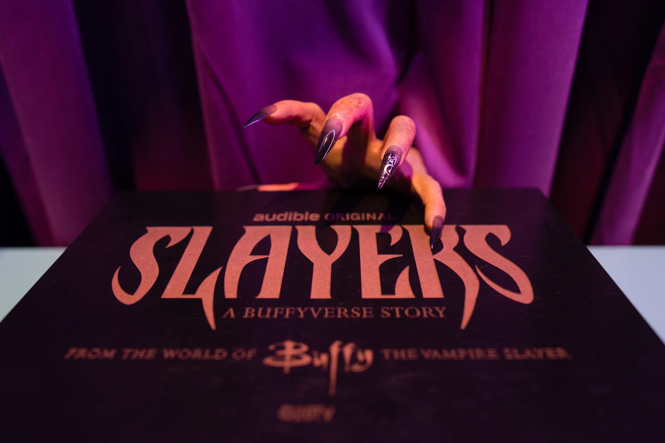 A gloved hand reaching for the Slayers box set under violet light at the Audible event