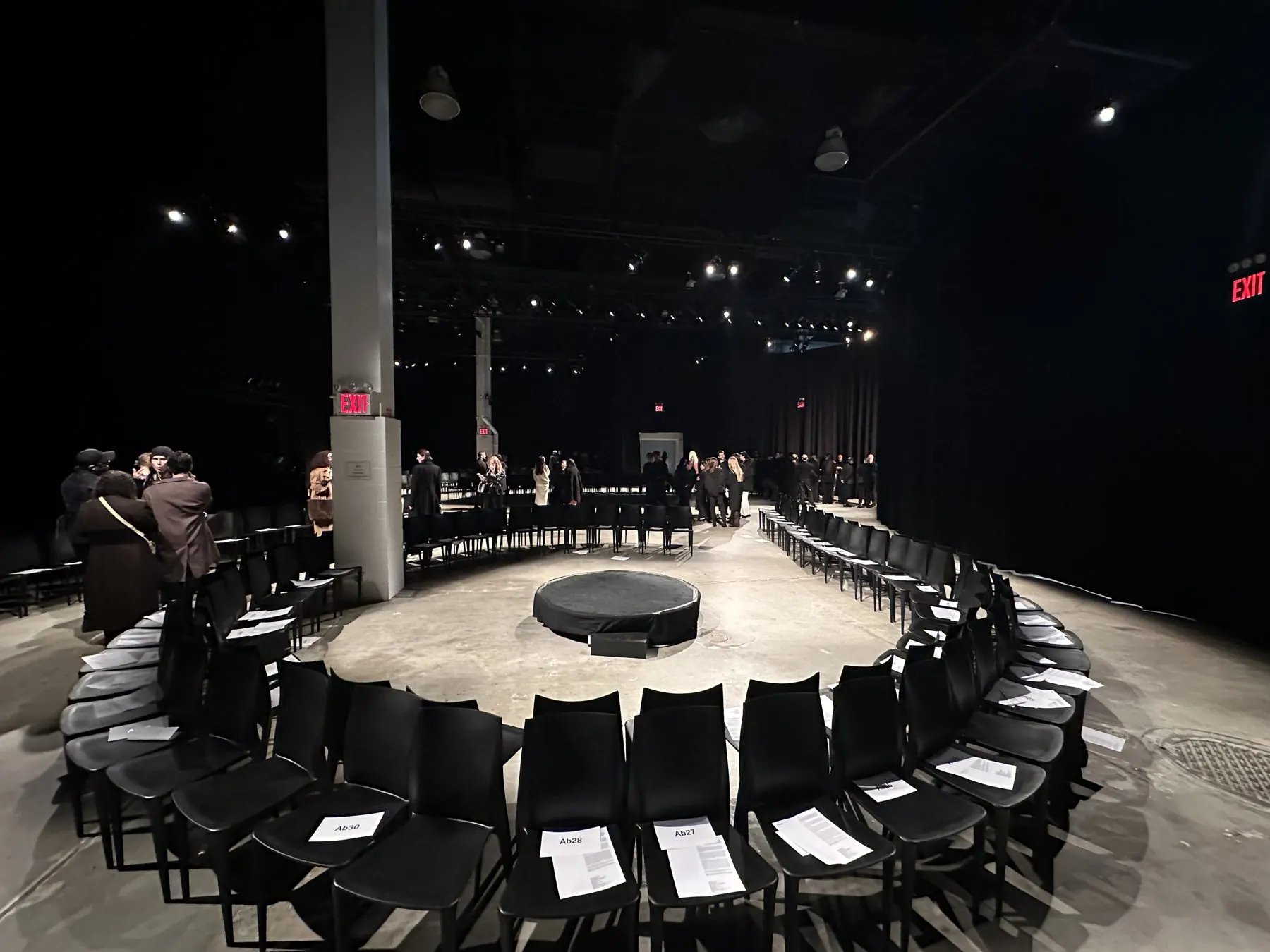Fashion presentation set in the round: rows of black chairs circling a center plinth